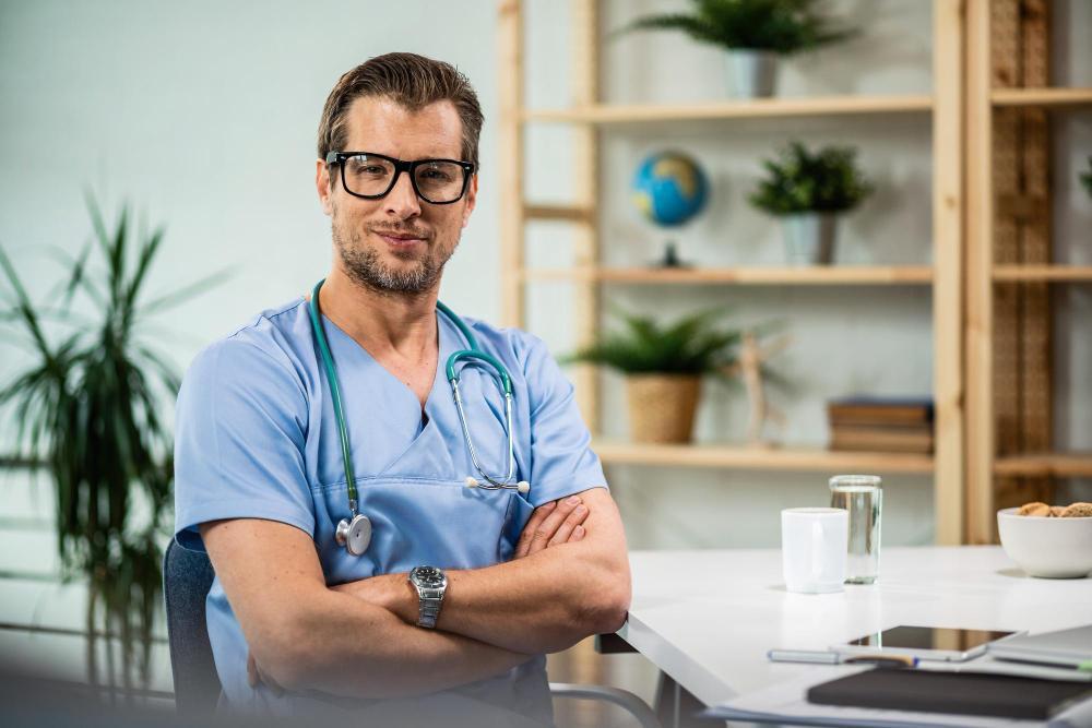 A male nurse dressed in blue scrubs stops to have his photograph taken