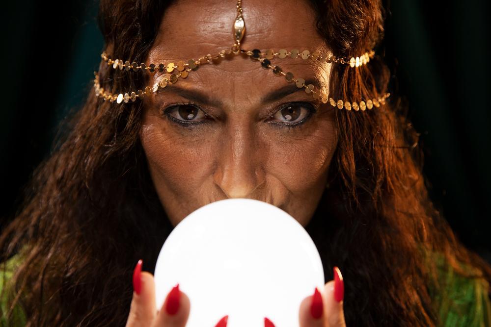 Woman dressed in a golden headdress holds a white crystal ball