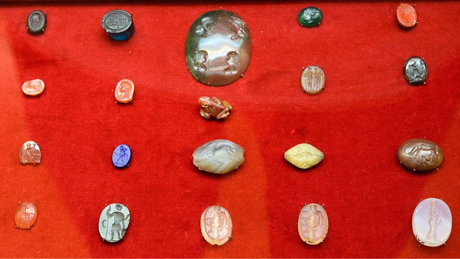 A red table displaying various Roman gems, coins and artifacts of varying sizes and color