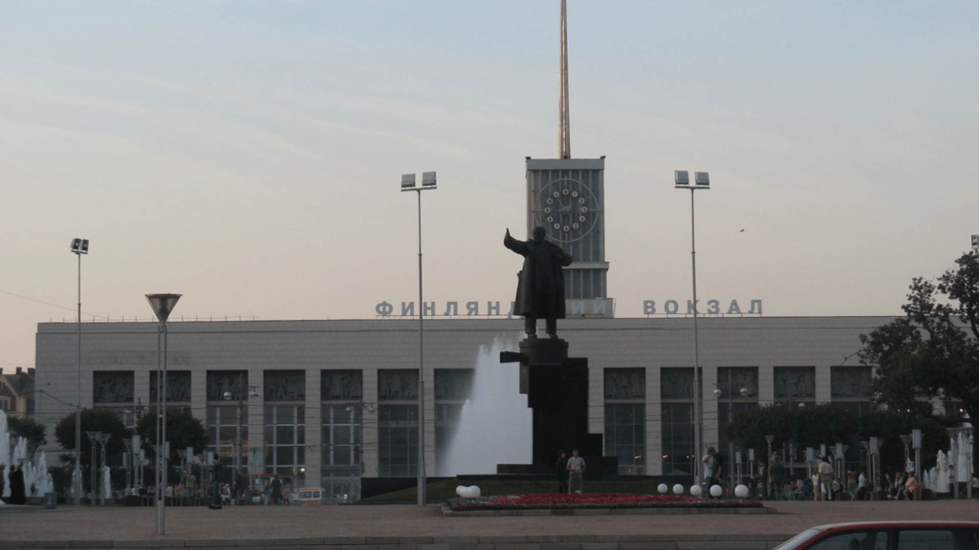 The statue of Lenin outside St. Petersburg's Finland Station. The station and a fountain can be seen behind the statue, with numerous people milling about.