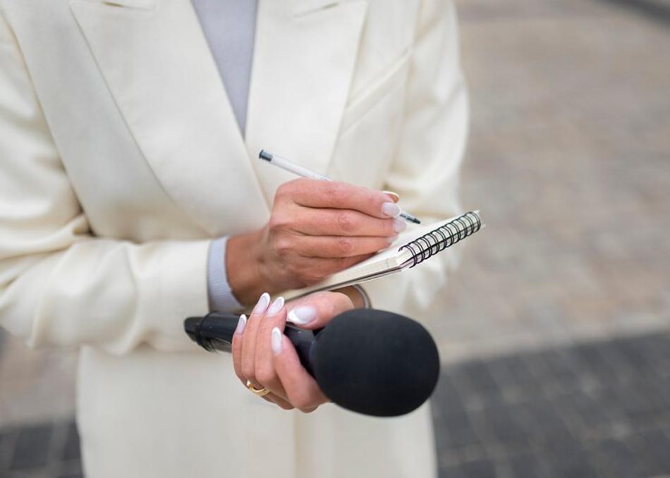 A woman dressed in a white coat is pictured as she holds a mic and writes down notes