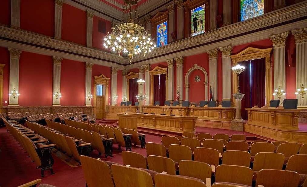 A chandelier handing over rows of wooden seats and a large wooden bench in a tall room with red painted walls and stained glass windows