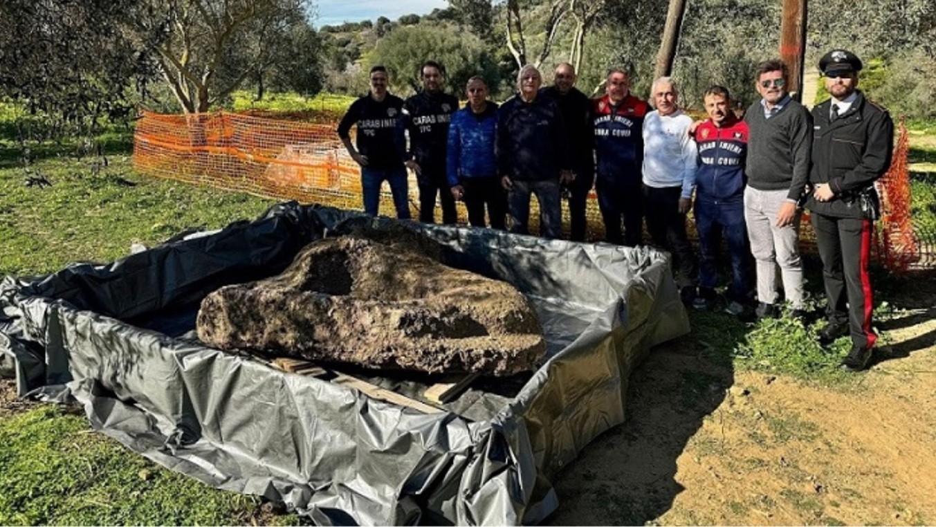 A line of people standing behind a large marble artifact on the ground before them.