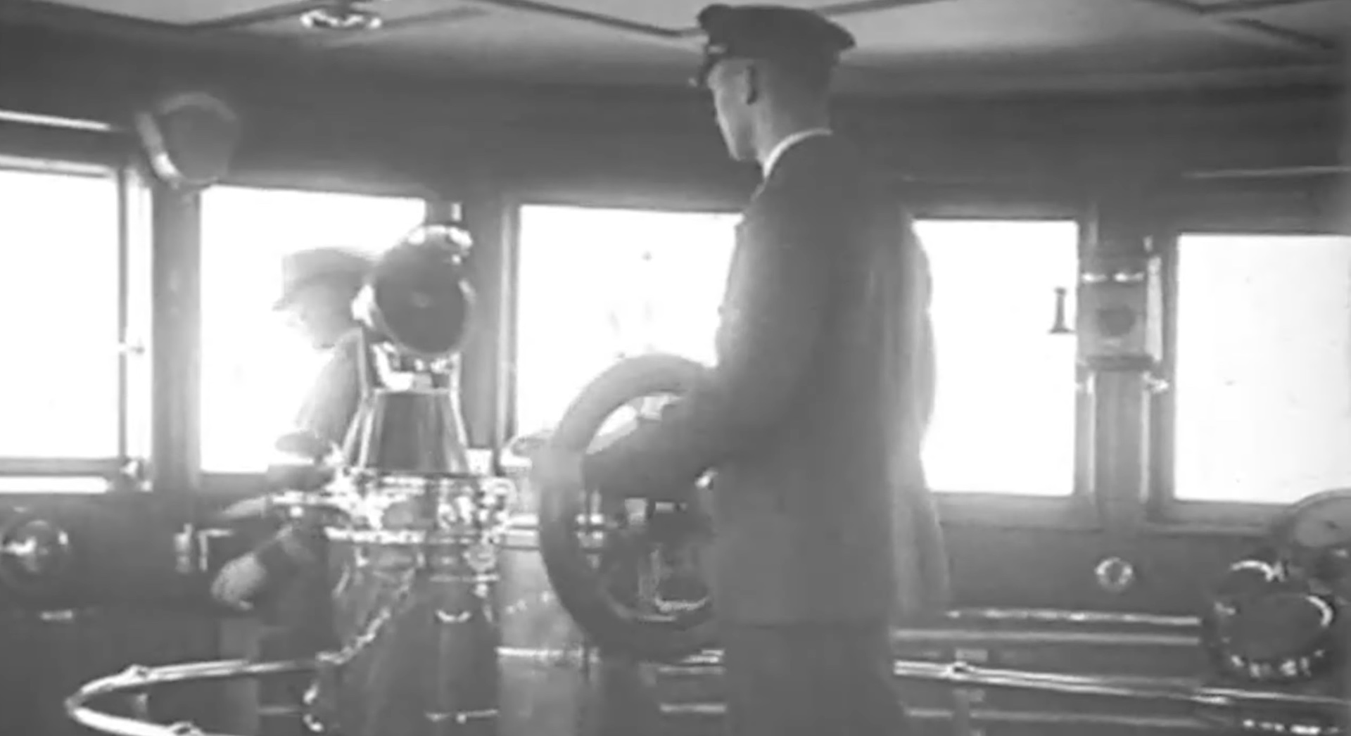 A gray scale image of a captain steering a ship in the water