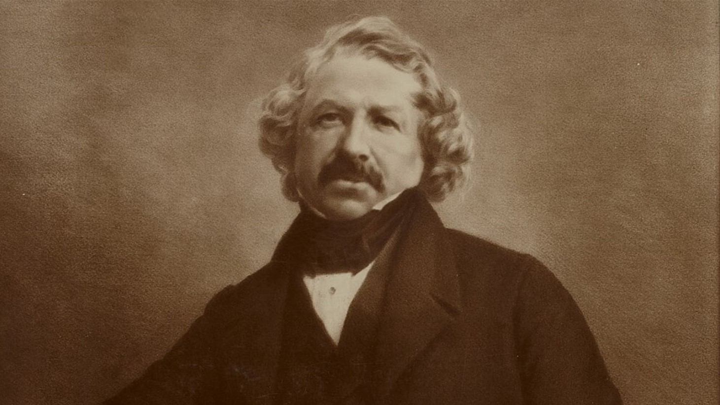 Sepia-toned portrait of Louis Daguerre, the inventor of the daguerreotype process in photography. He is depicted with curly shoulder-length hair and a prominent mustache, wearing a dark jacket and a high-collared shirt with a cravat