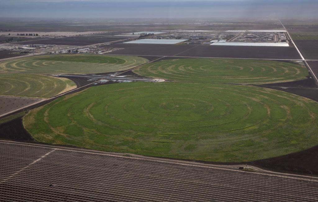 A circular irrigation system for growing hay and alfalfa is viewed from above and in close proximity to Tulare Lake