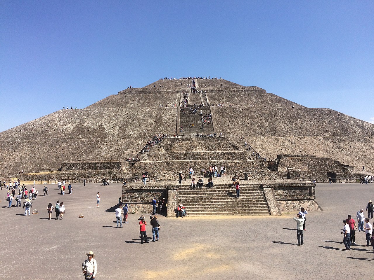 Teotihuacan's Pyramid of the Sun, photographed from the front in broad daylight. People are walking toward and up the steps on the pyramid.