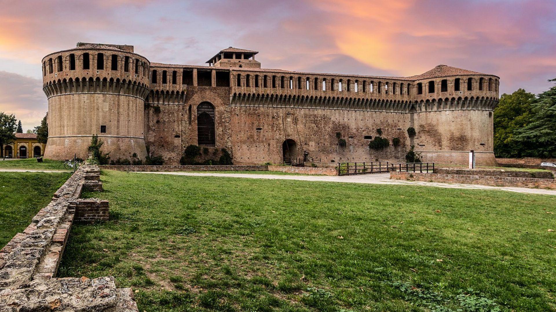 The walls of a European fortress with two round towers on a green field.