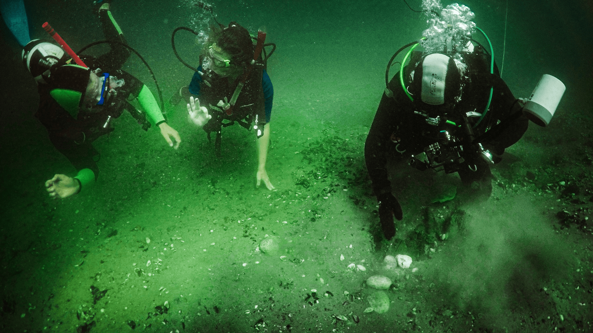 Three people at the seafloor in scuba diving suits.