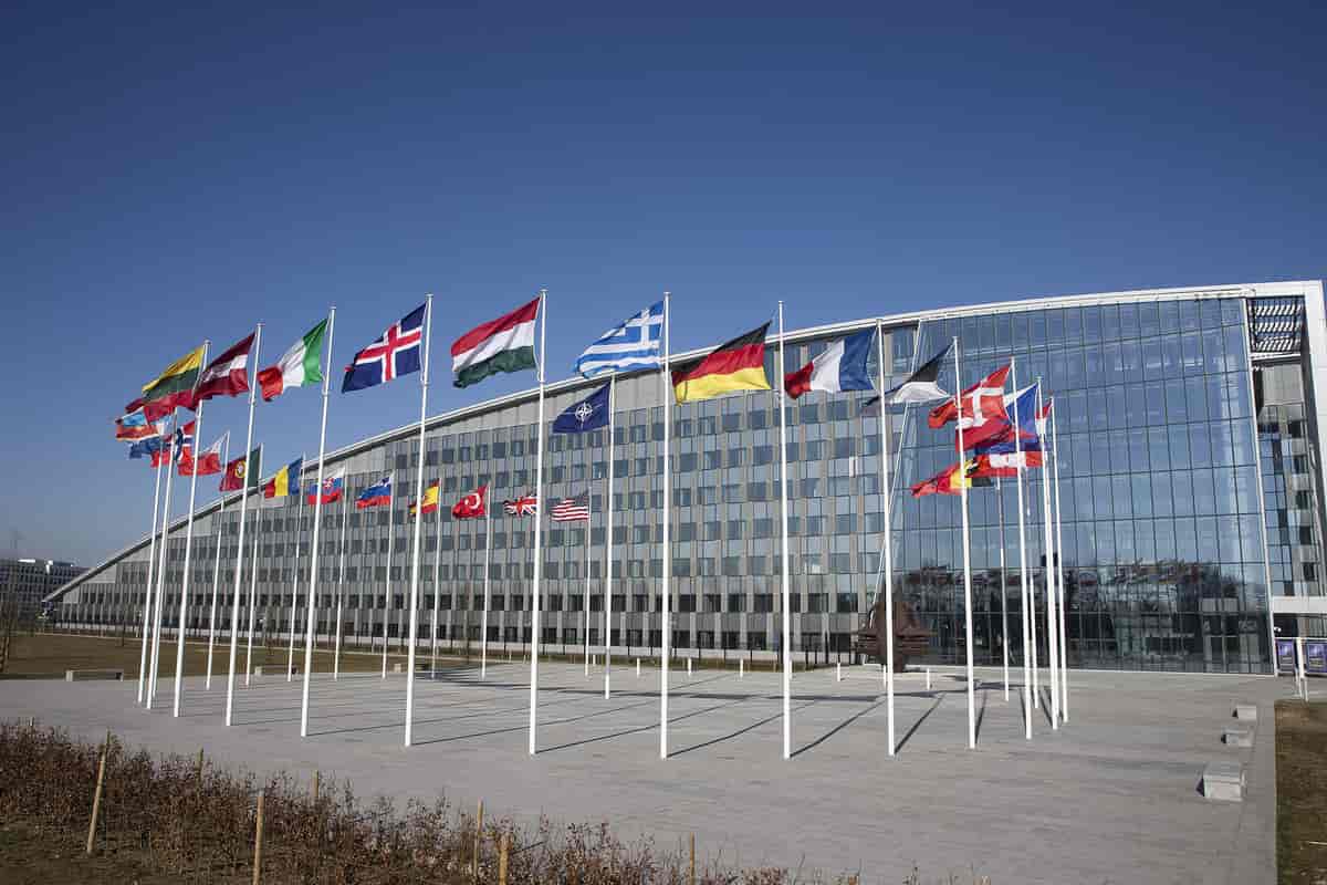 Several nation's flags in a circle waving in the wind in front of a glass building