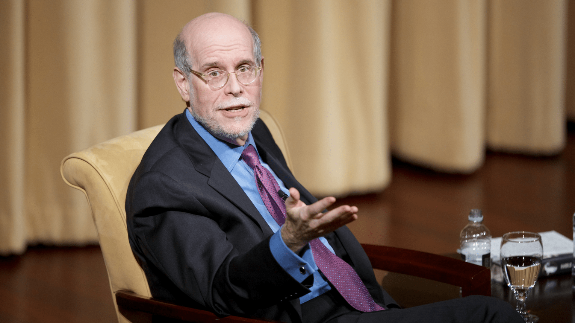 Author and historian Harold Holzer sitting in a chair in a suit speaking during a discussion about a 2014 book on Lincoln.