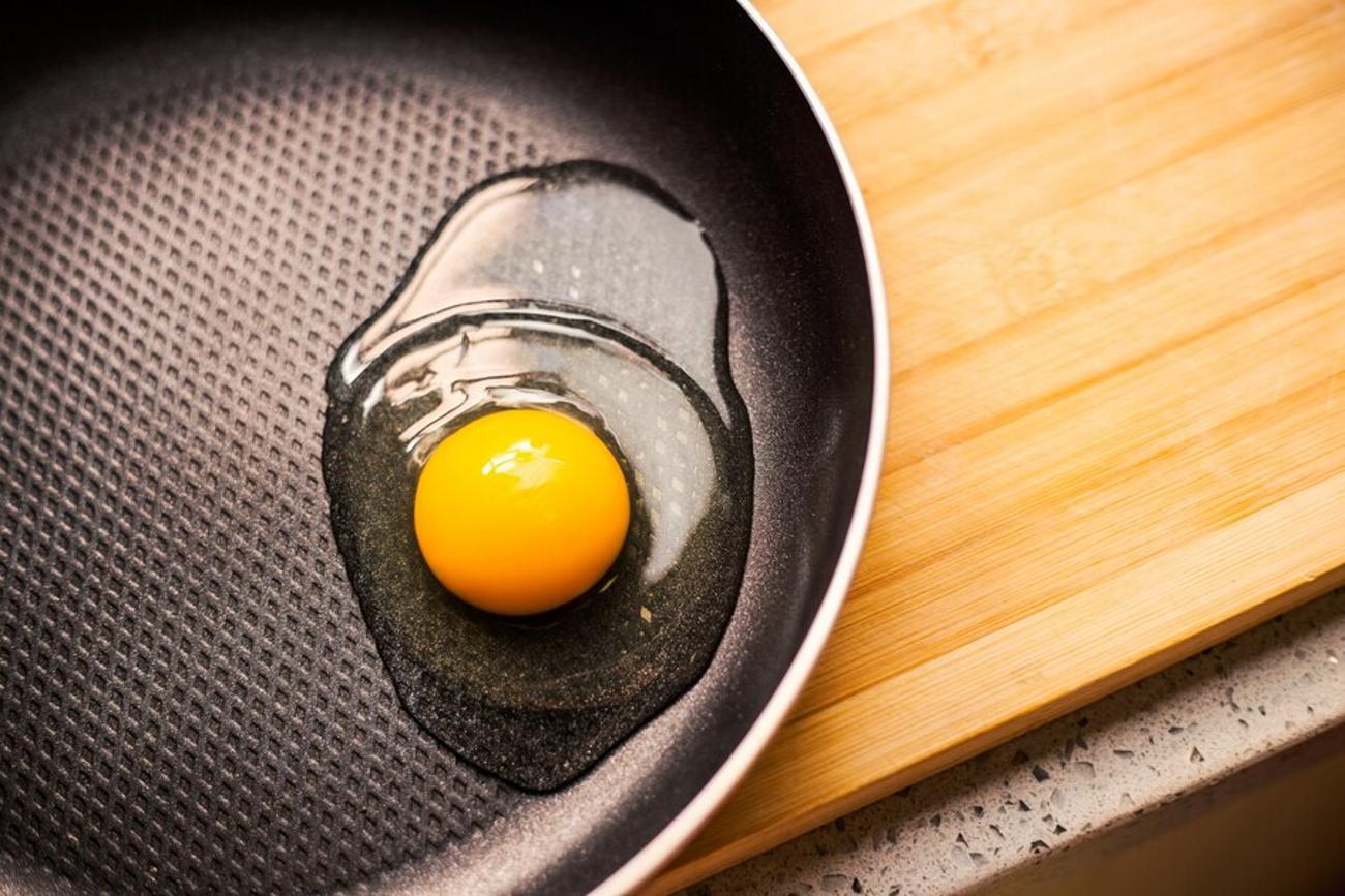 Egg cracked open into a pan on a wooden chopping board