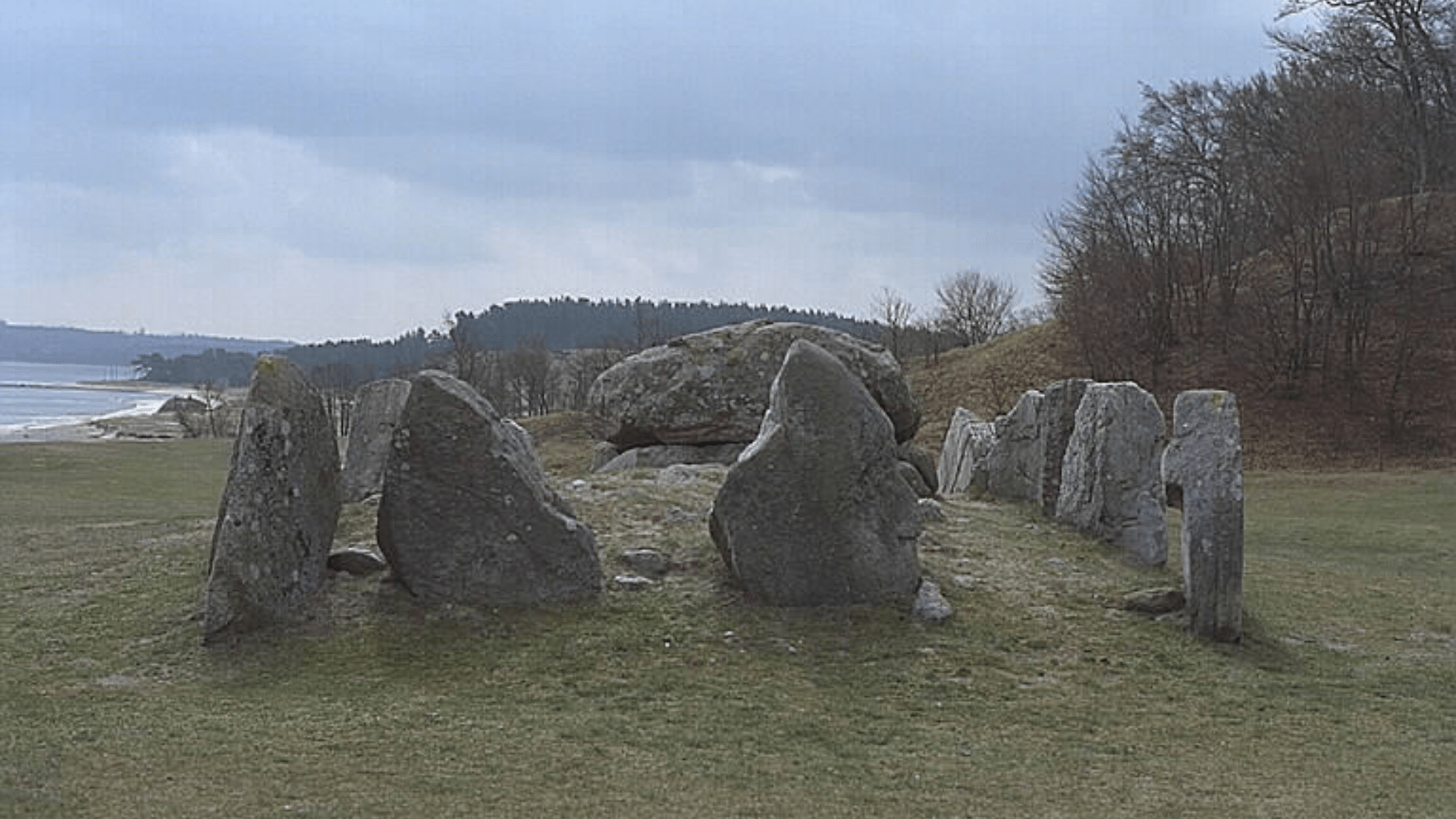 A Swedish dolmen featuring a rind of rocks standing on end in the ground around the tomb.