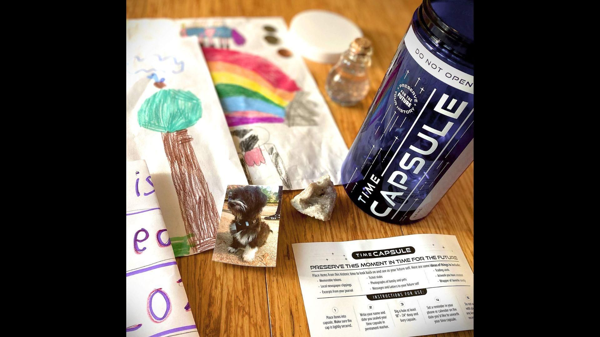 A time capsule kit with children’s drawings, a picture of a dog, and a rock ready to be placed inside
