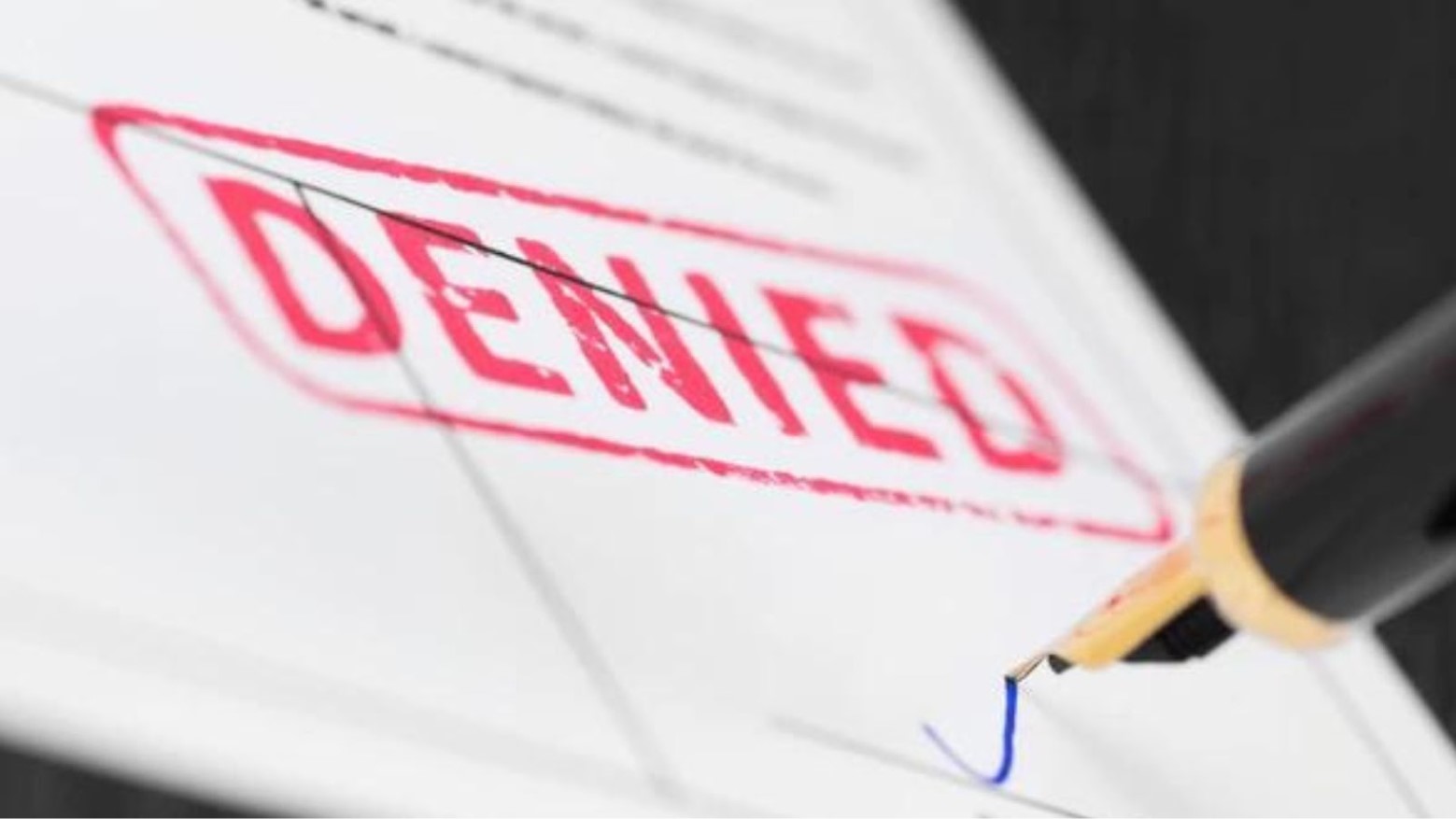 Close-up of a pen signing paperwork that reads “Denied”