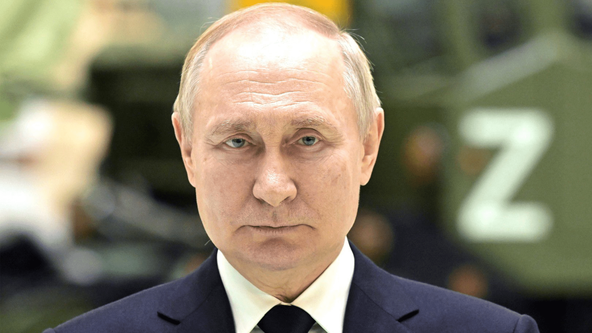 A headshot of Putin wearing a suit. He is expressionless.