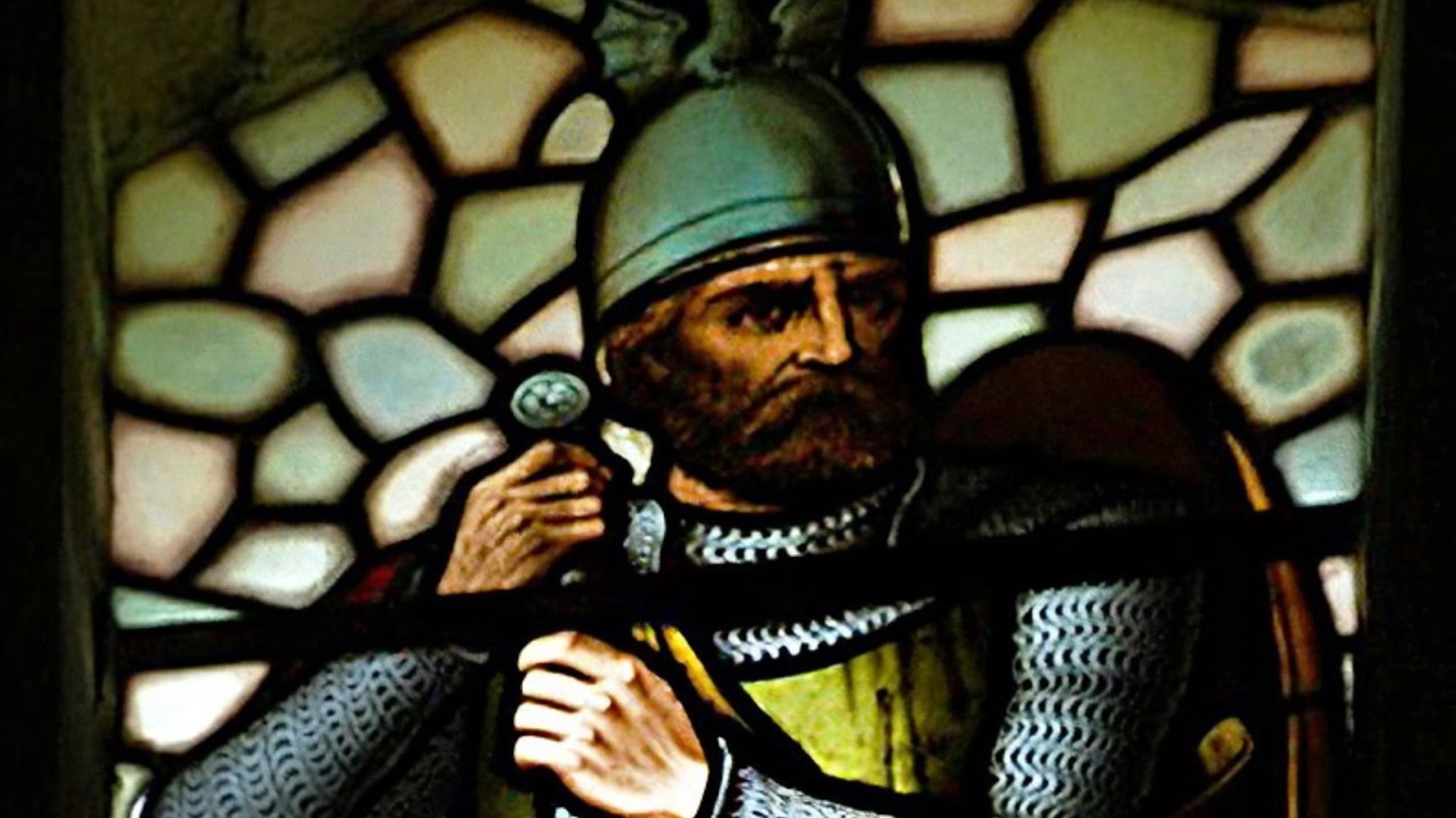 A stained glass image portraying William Wallace in a historic setting. He is depicted with a stern, bearded face, wearing a chainmail coif and armor, with a sword slung over his shoulder