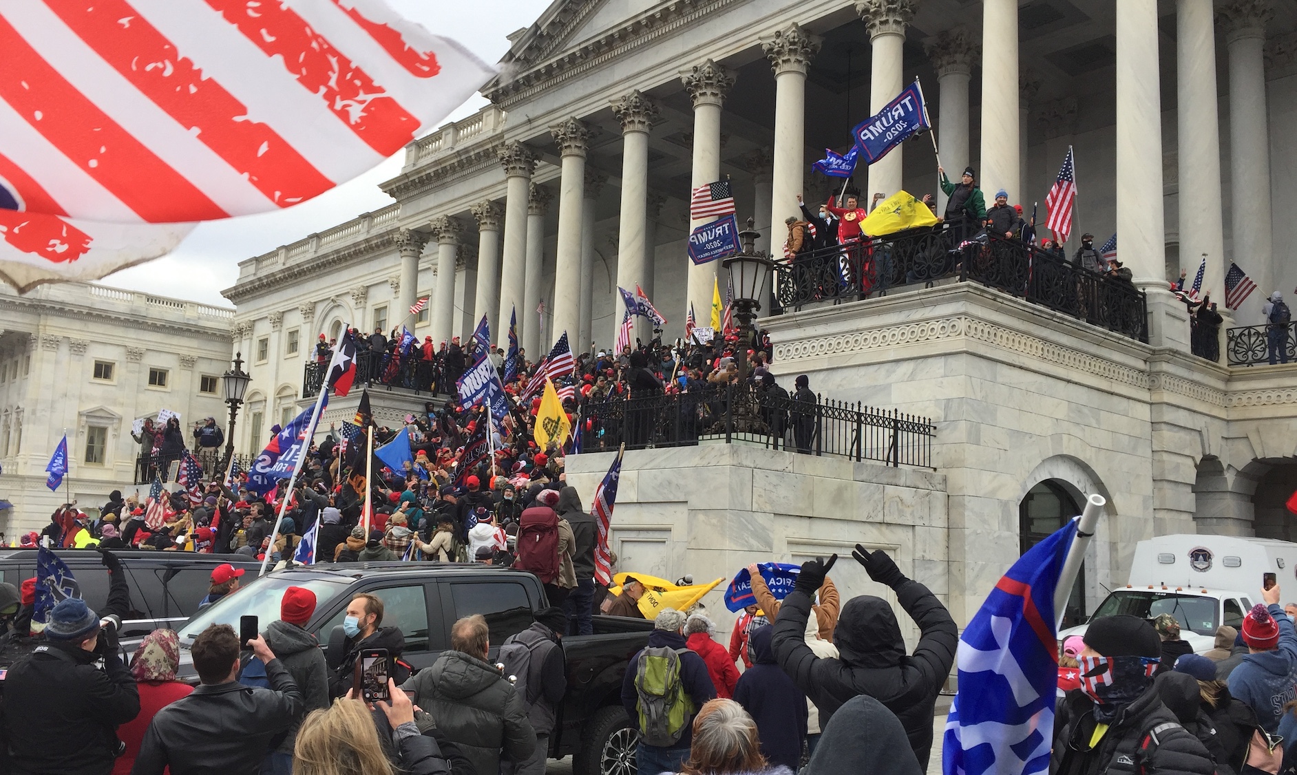 A large group of people waving supporter flags and American flags while loitering on the steps of the U.S. capitol building