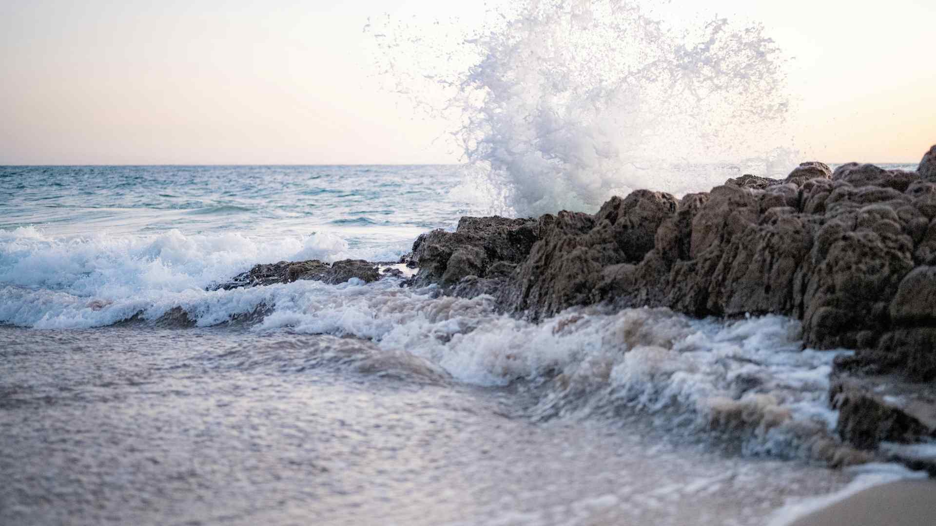 Waves crash against some rocks on a beach.