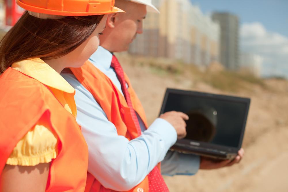 A man and a woman dressed in high-vis gear stare at a laptop next to a site
