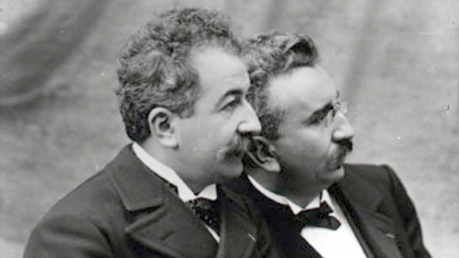 Black and white historical photograph of the Lumière brothers, Auguste and Louis, pioneers of early cinema. They are shown in profile, facing to the right, with their faces close together