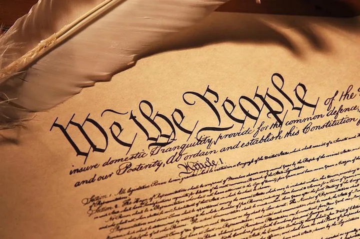 The U.S. constitution reading "We the People" in large cursive text and a feathered quill resting on top of the text