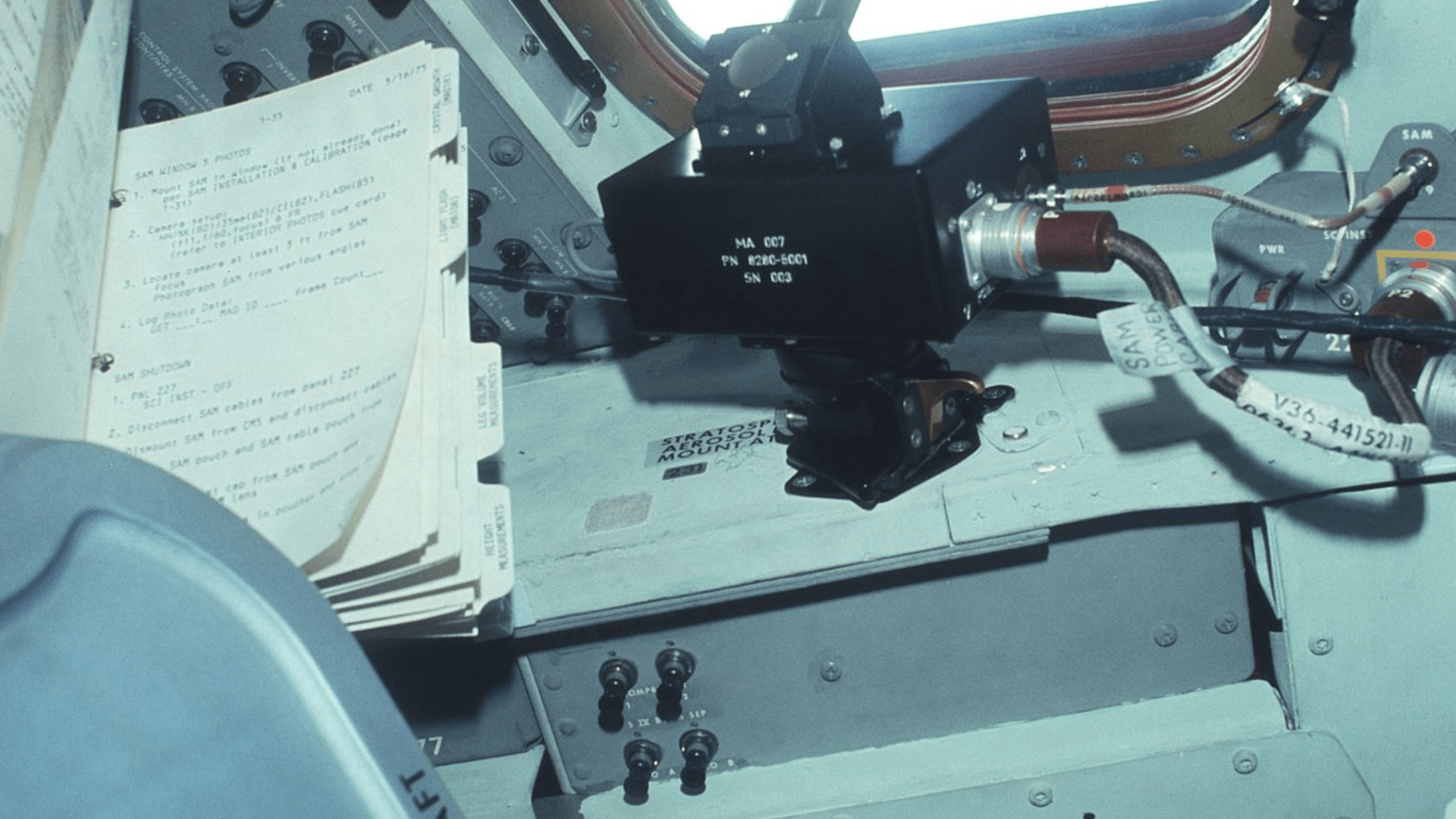 A piece of equipment for measuring stratospheric aerosols next to a file filled with typewritten papers and tabbed separators.