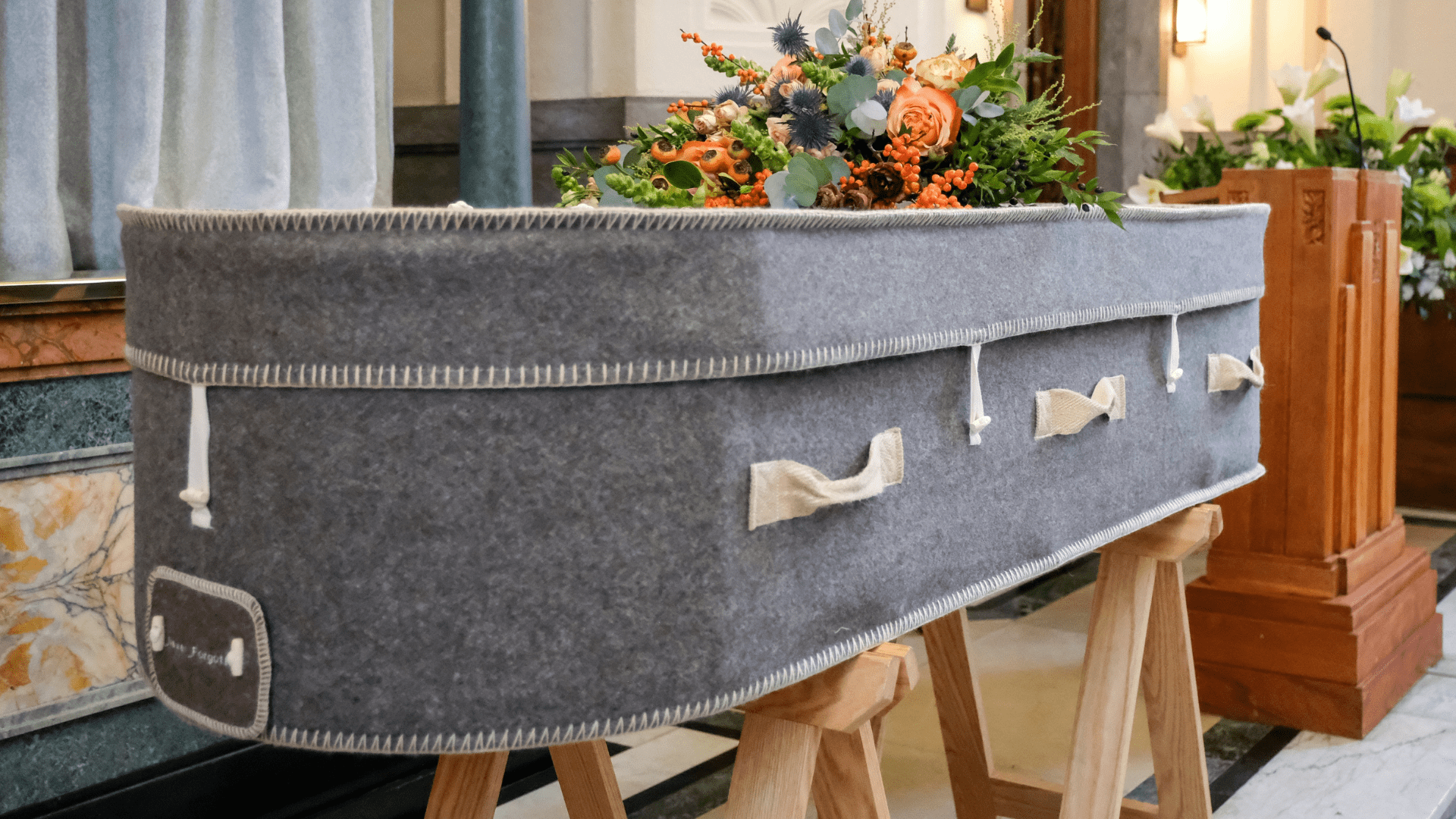 A gray coffin sitting on wooden stands with a flower bouquet on top of it.