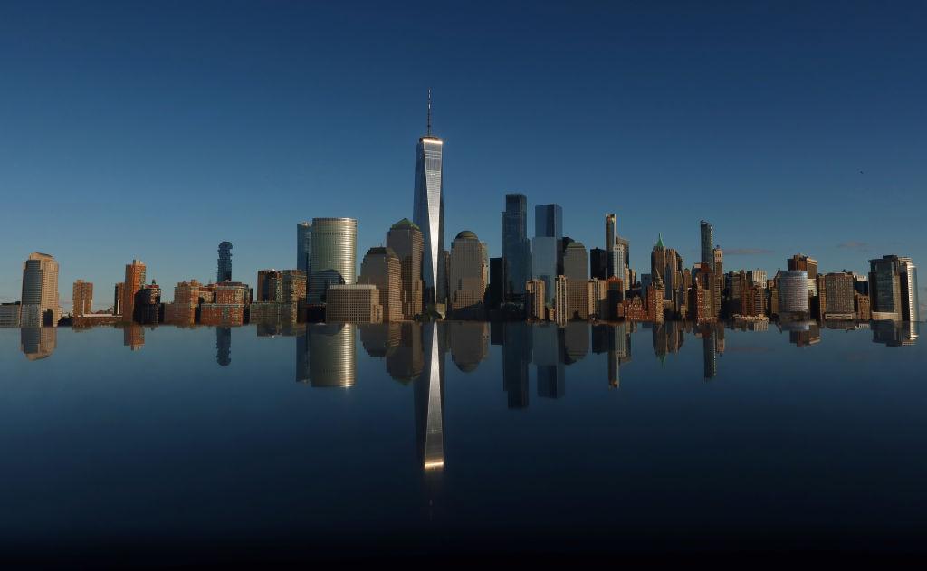 The skyline of lower Manhattan and One World Trade Center in New York City is reflected on the top of a monument along the Hudson River