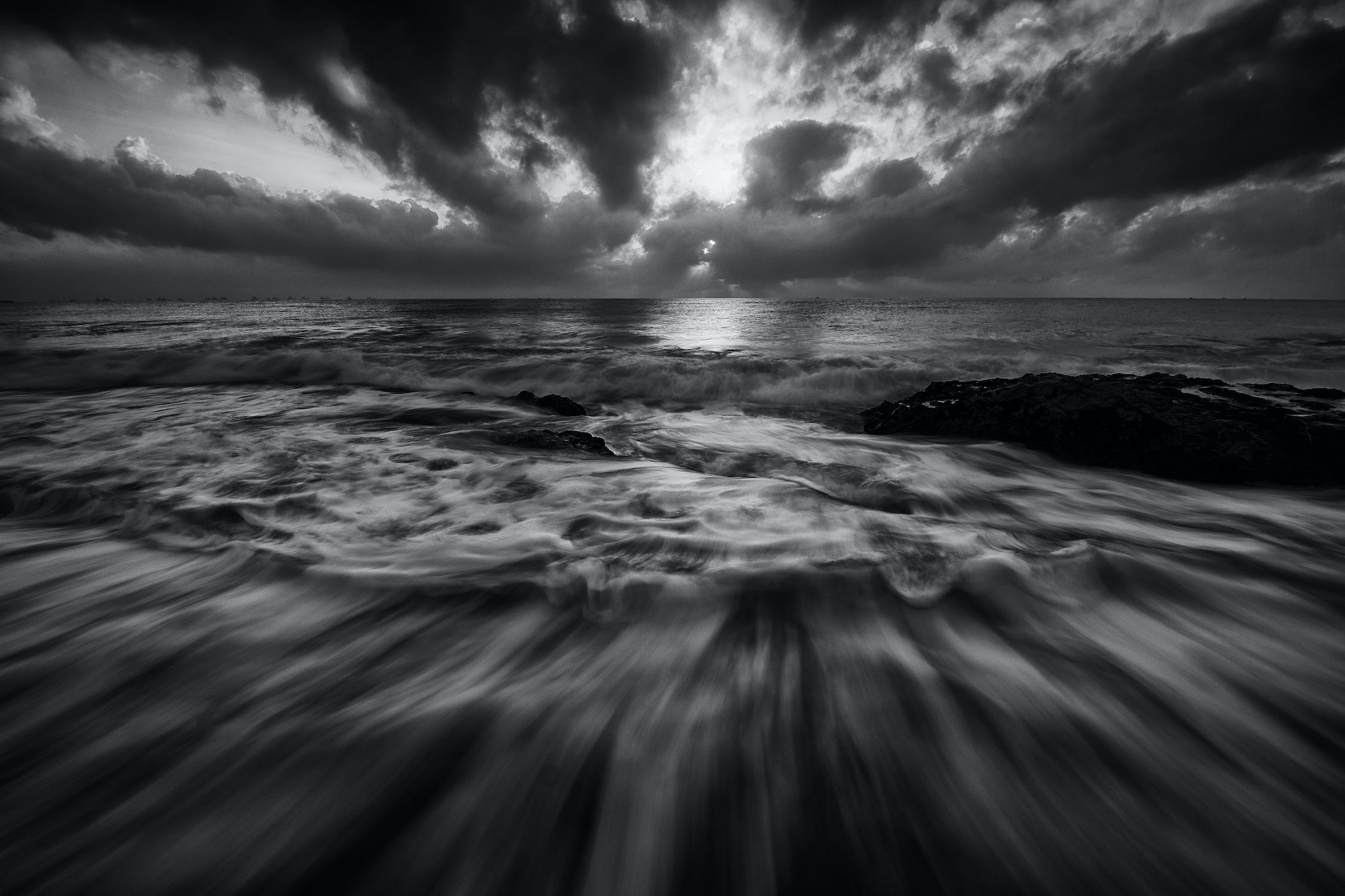 A greyscale image of the ocean tide pulling out under a cloudy sky