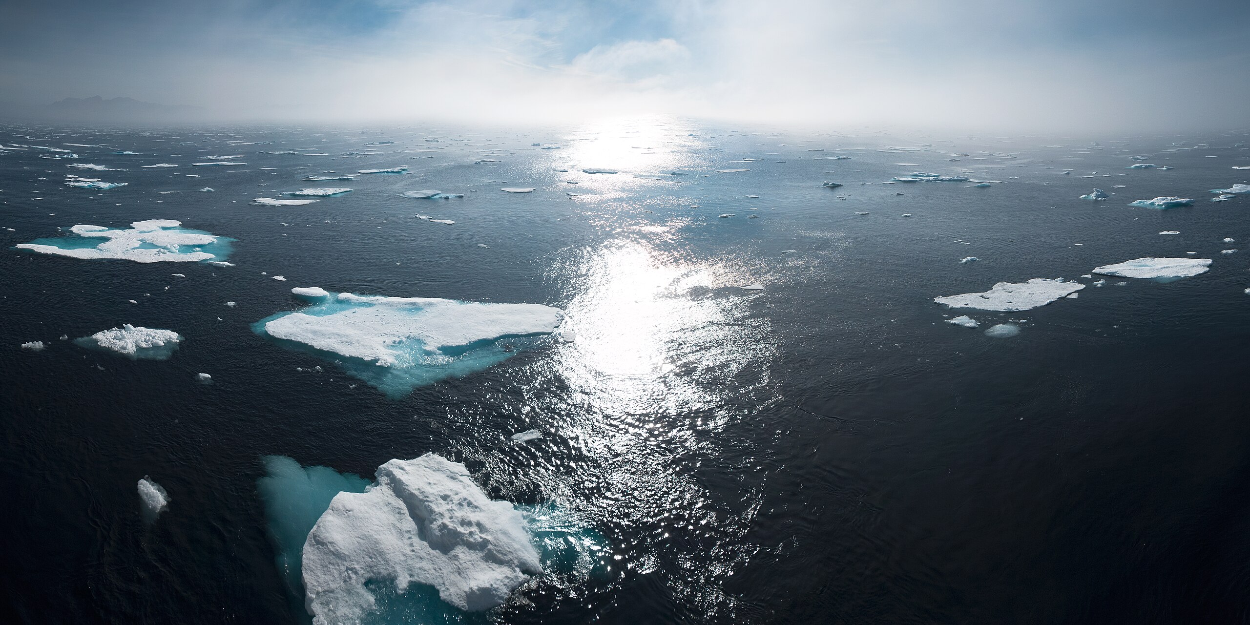 The sun sets over the Greenland ocean. Chunks of ice re seen floating about and sticking out f the water.