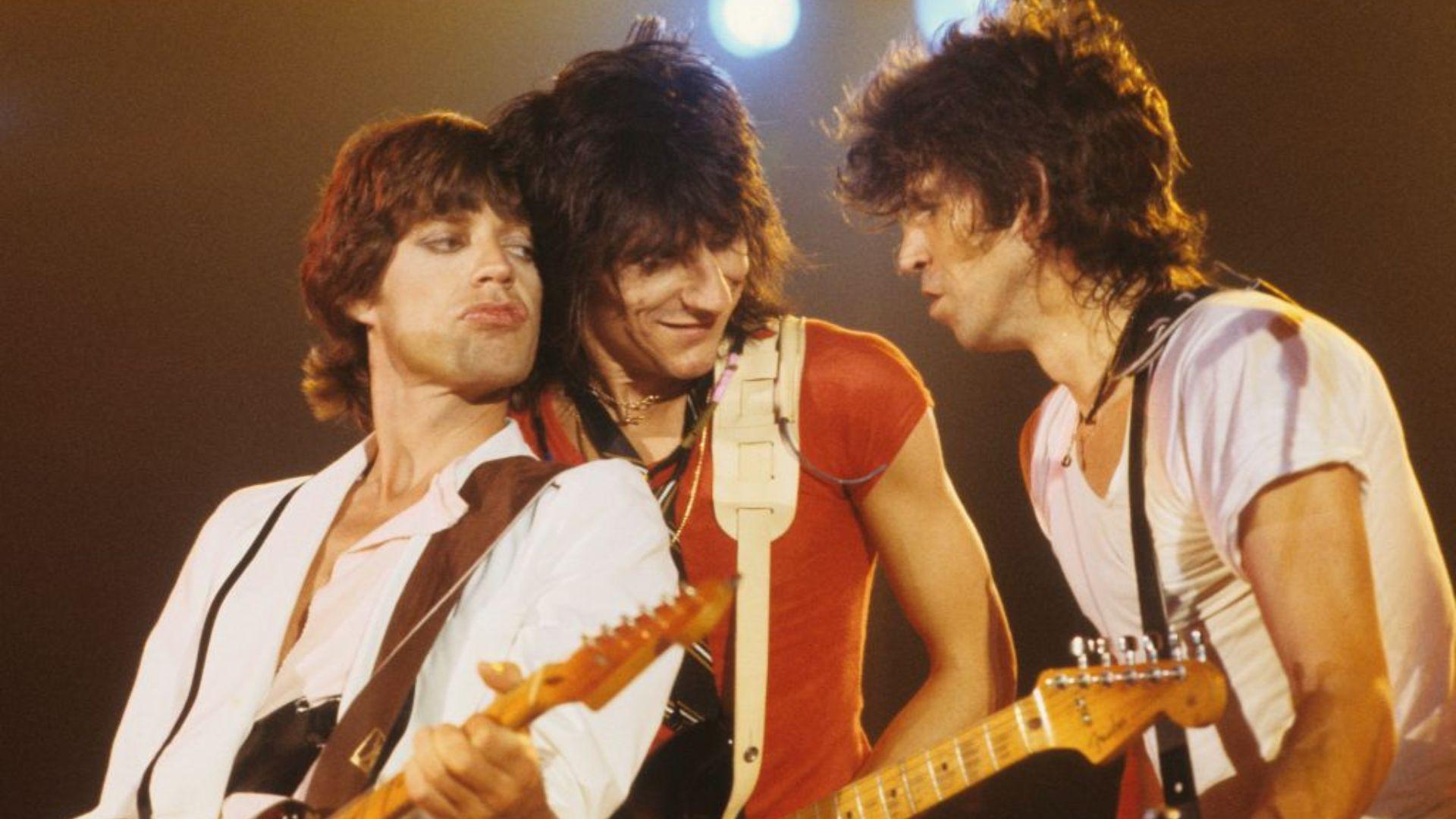 Mick Jagger, Ronnie Wood and Keith Richards on stage. All three have guitars and are standing close to each other