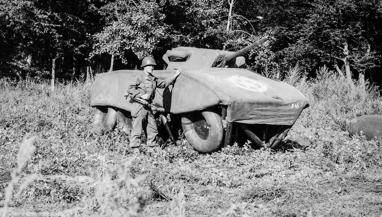 A gray scale image of an American solider standing next to a tank made from cardboard