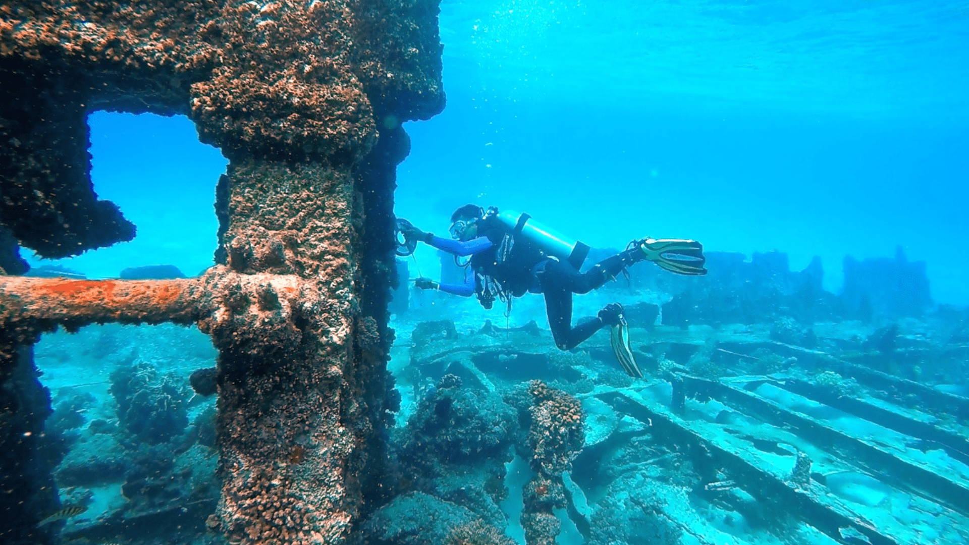 A shipwrecked engine being measured by an underwater archaeologist wearing a scuba diving suit.