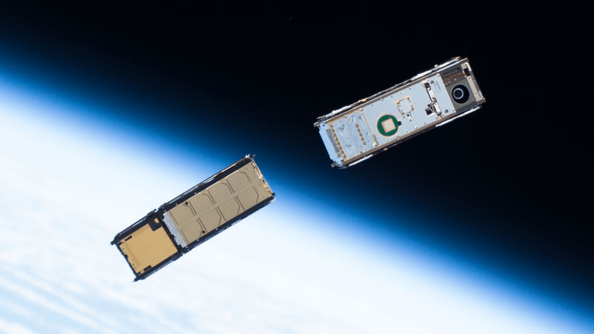 Two CubeSat satellites in orbit above the Earth, which appears as a glowing blue mass cutting diagonally through half of the image.
