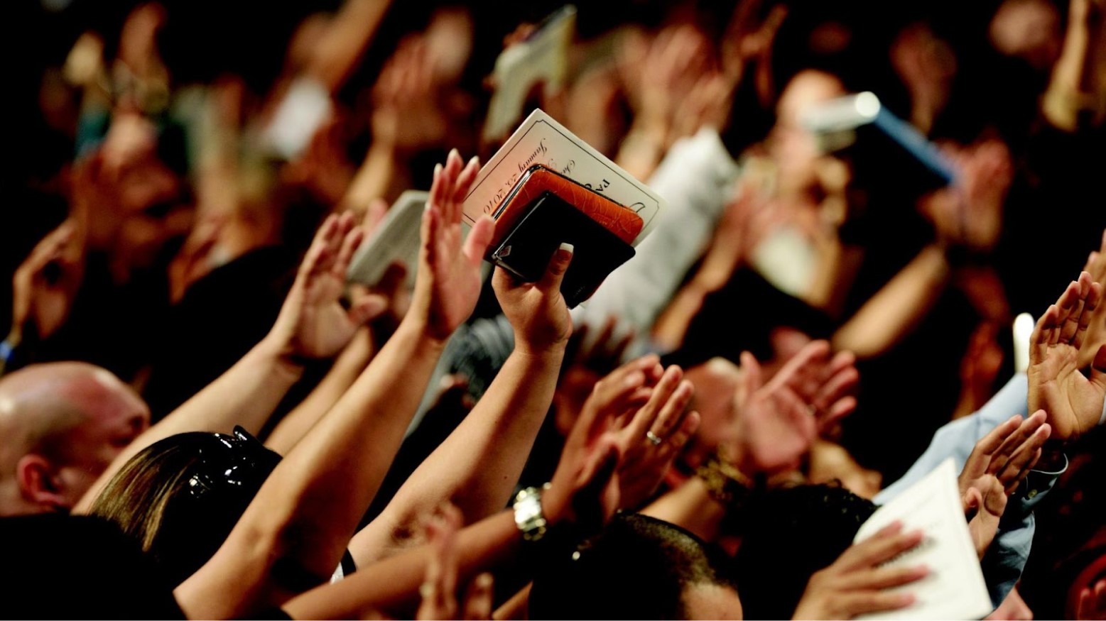 People of all ages and genders in a large group hold their hands up in prayer