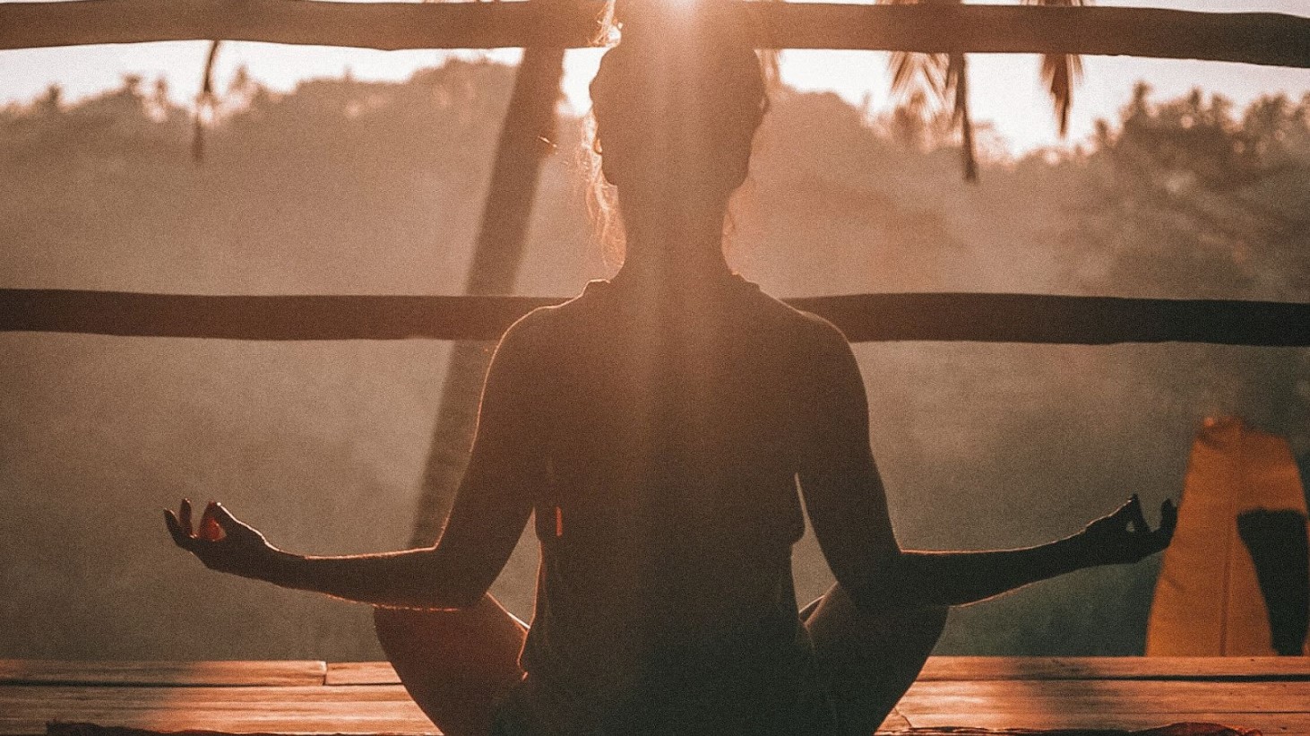 The silhouette of a person is captured in a meditative pose, backlit by the light of the rising sun