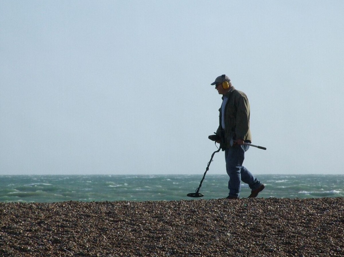 An image of a man walking along a beach with a metal detector in Britain