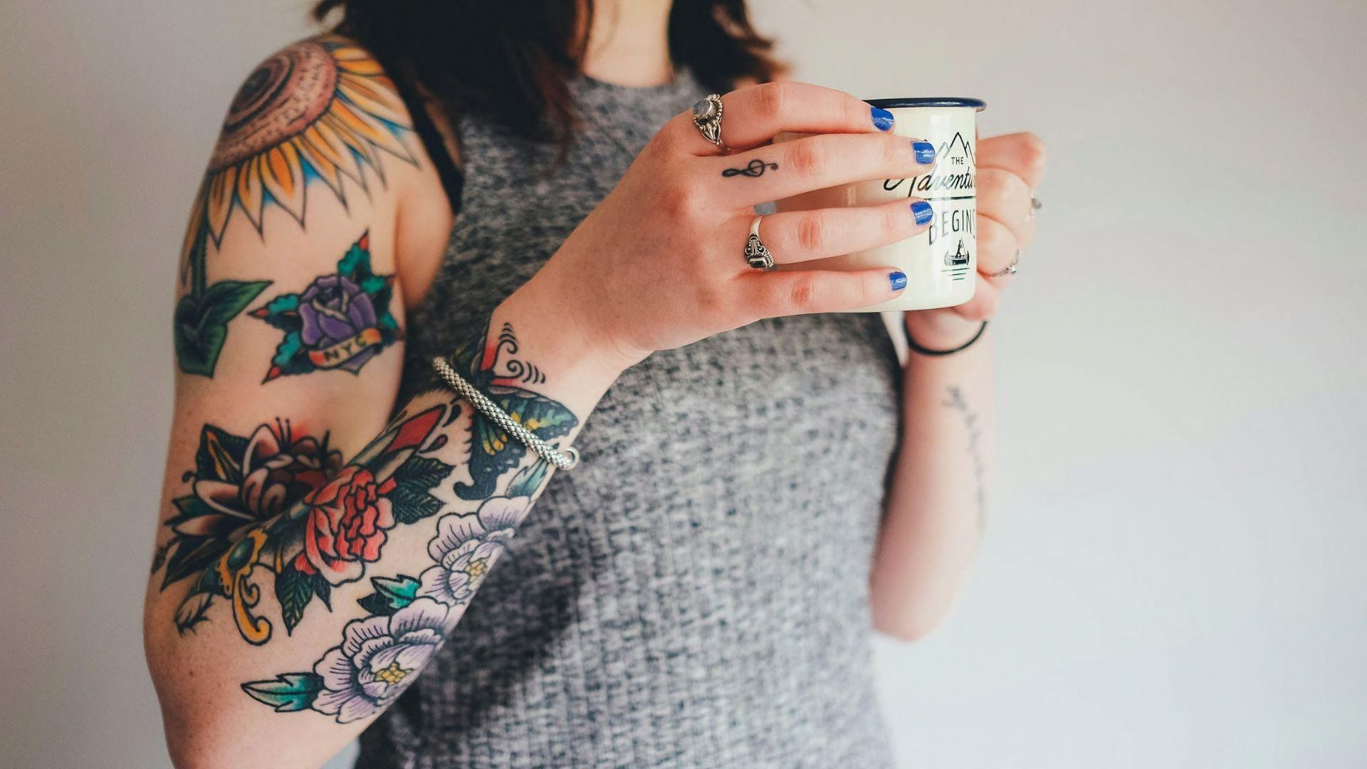 A woman holding a mug that has tattoos on her arm and fingers.