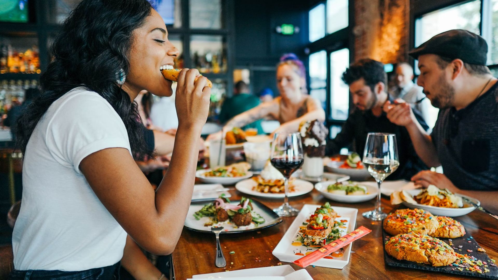 A group of men and women sat around a table eating food. There is food and wine on the table.