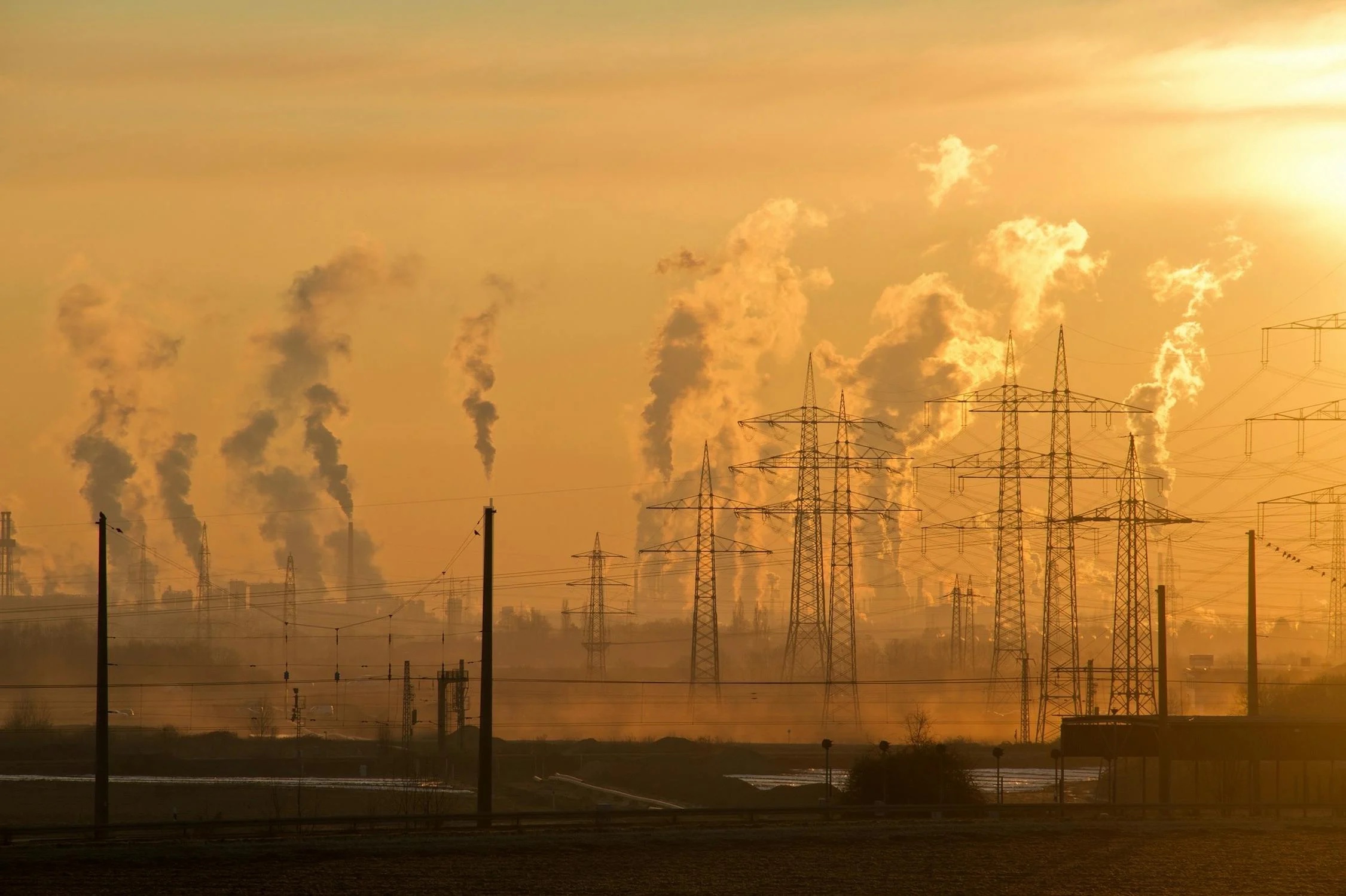 Electric towers in front of a factory with smoke coming out during a sunset