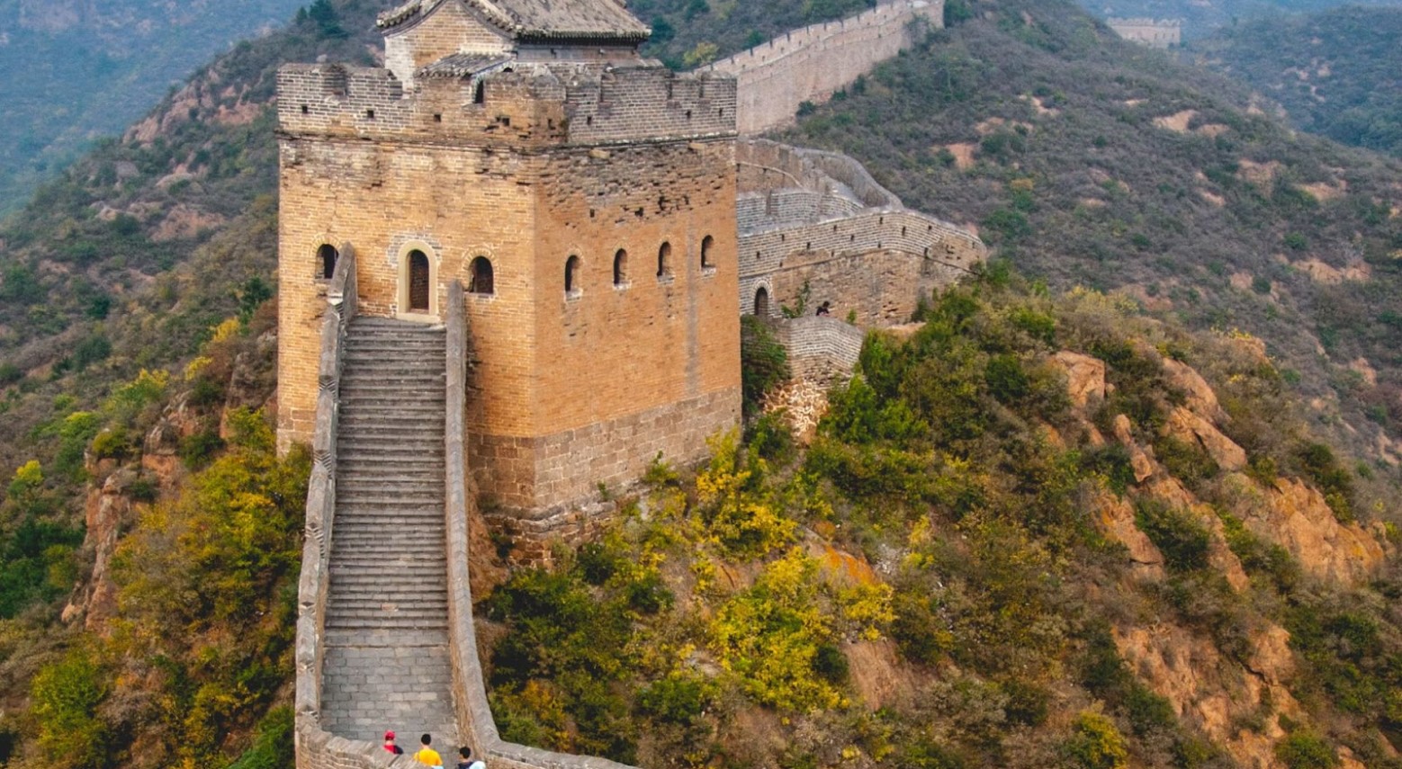 An image of the Great Wall of China. There are three people at the bottom of the wall who are walking upwards.