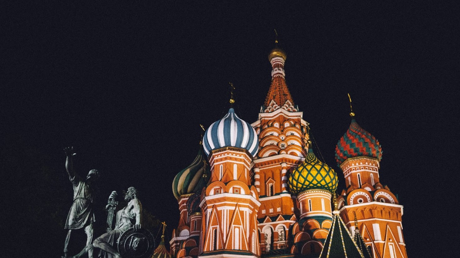 The colorful, illuminated domes of St. Basil's Cathedral in Moscow during nighttime, against a dark sky