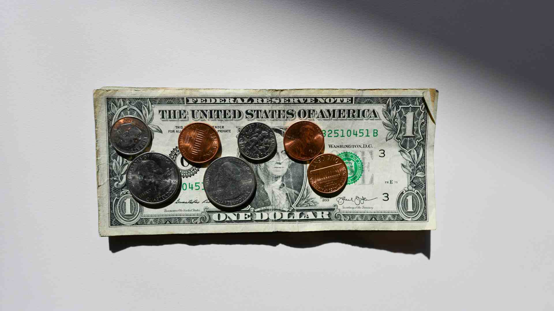 Small US coins sit on top of a one dollar bill.
