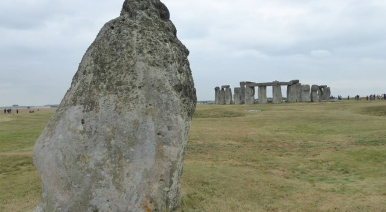 The heel stone at Stonehenge. In the background, the rest of the Stonehenge stones can be seen, with people surrounding them looking at the stones.
