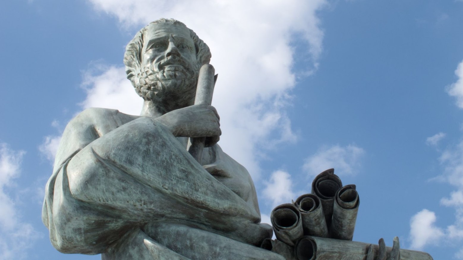 A statue of Aristotle outside underneath a cloudy blue sky.