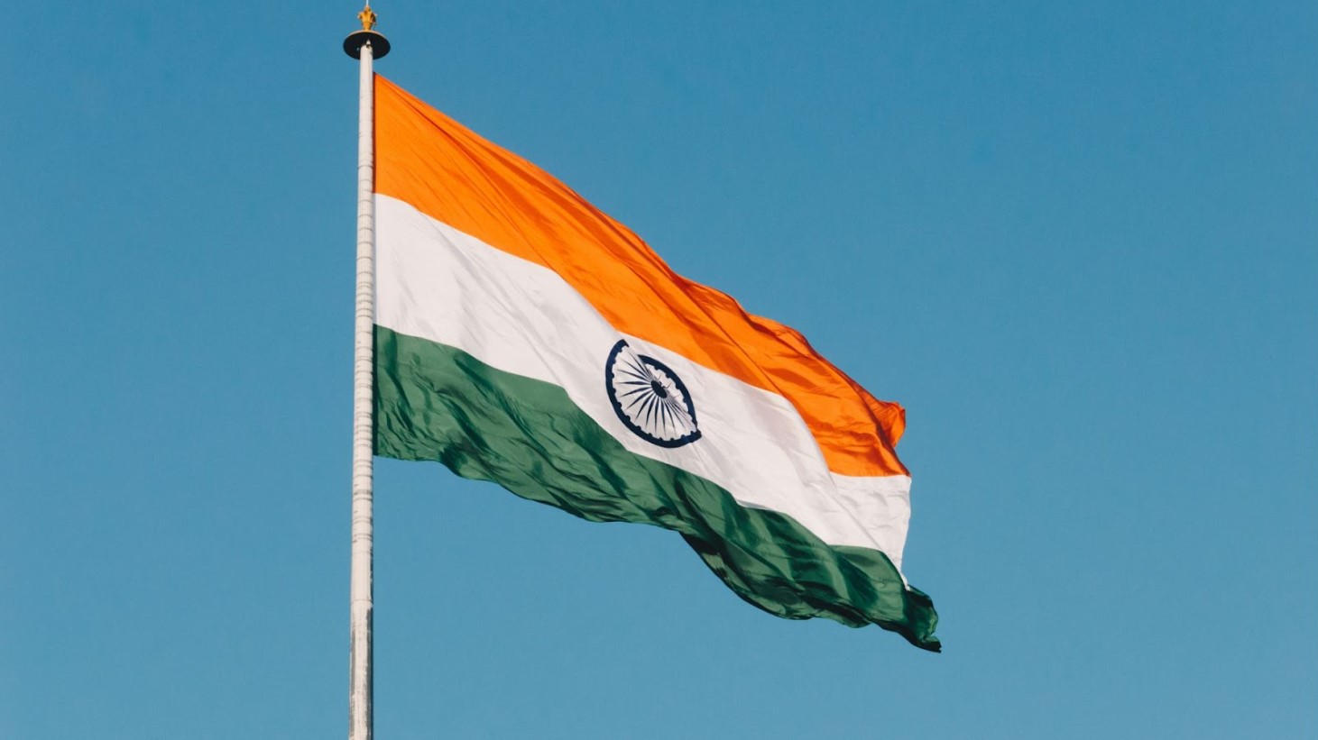 The national flag of India hoisted on a flagpole, waving in the wind with a clear blue sky in the background