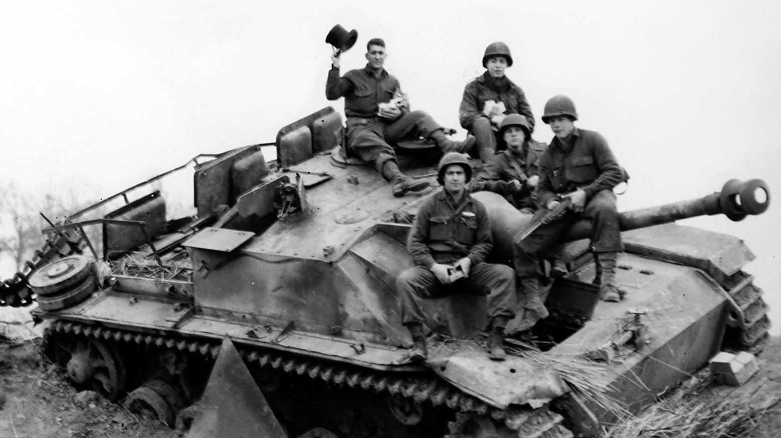 A black and white photo of U.S. soldiers sitting on a tank during World War II.