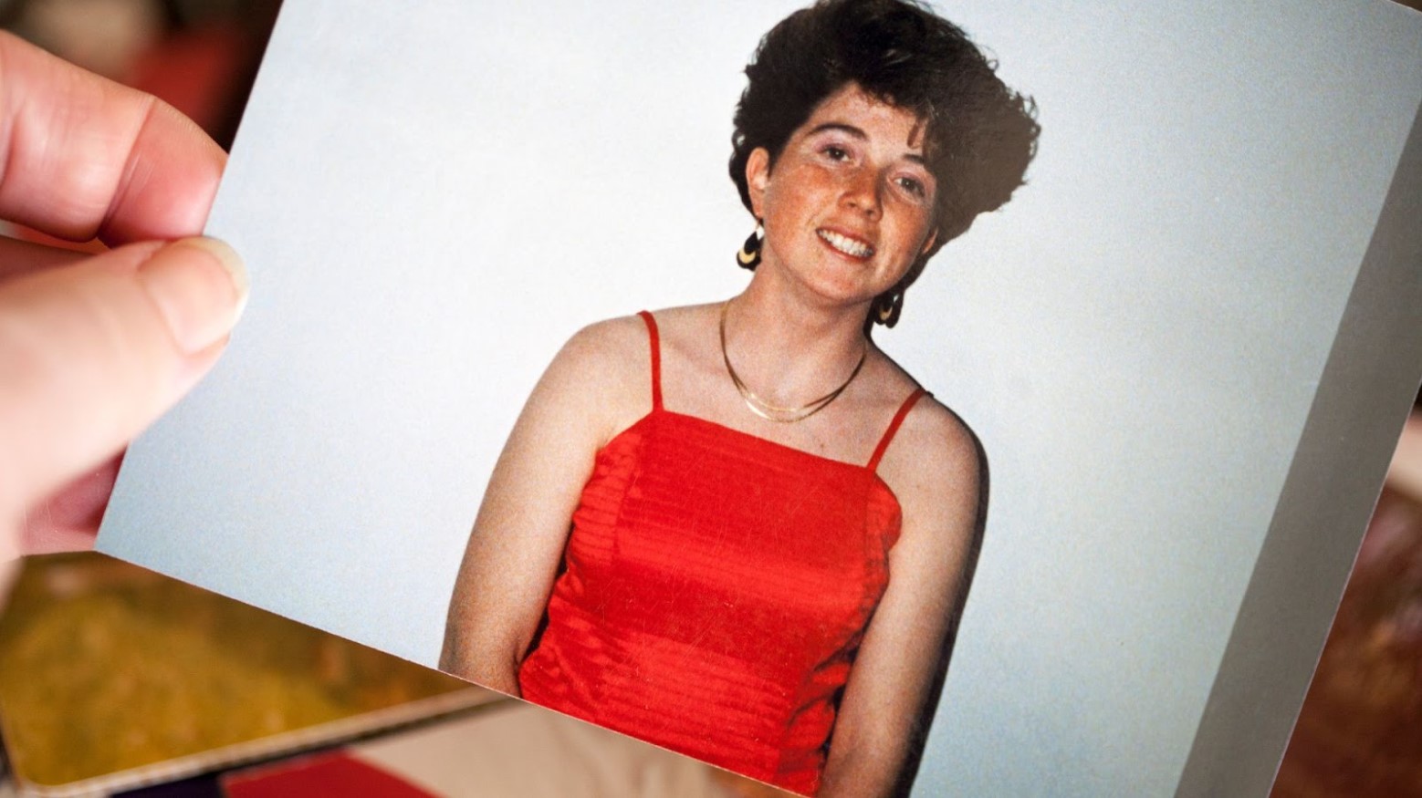 A photo shows a young woman in a red dress with curly hair and gold necklaces