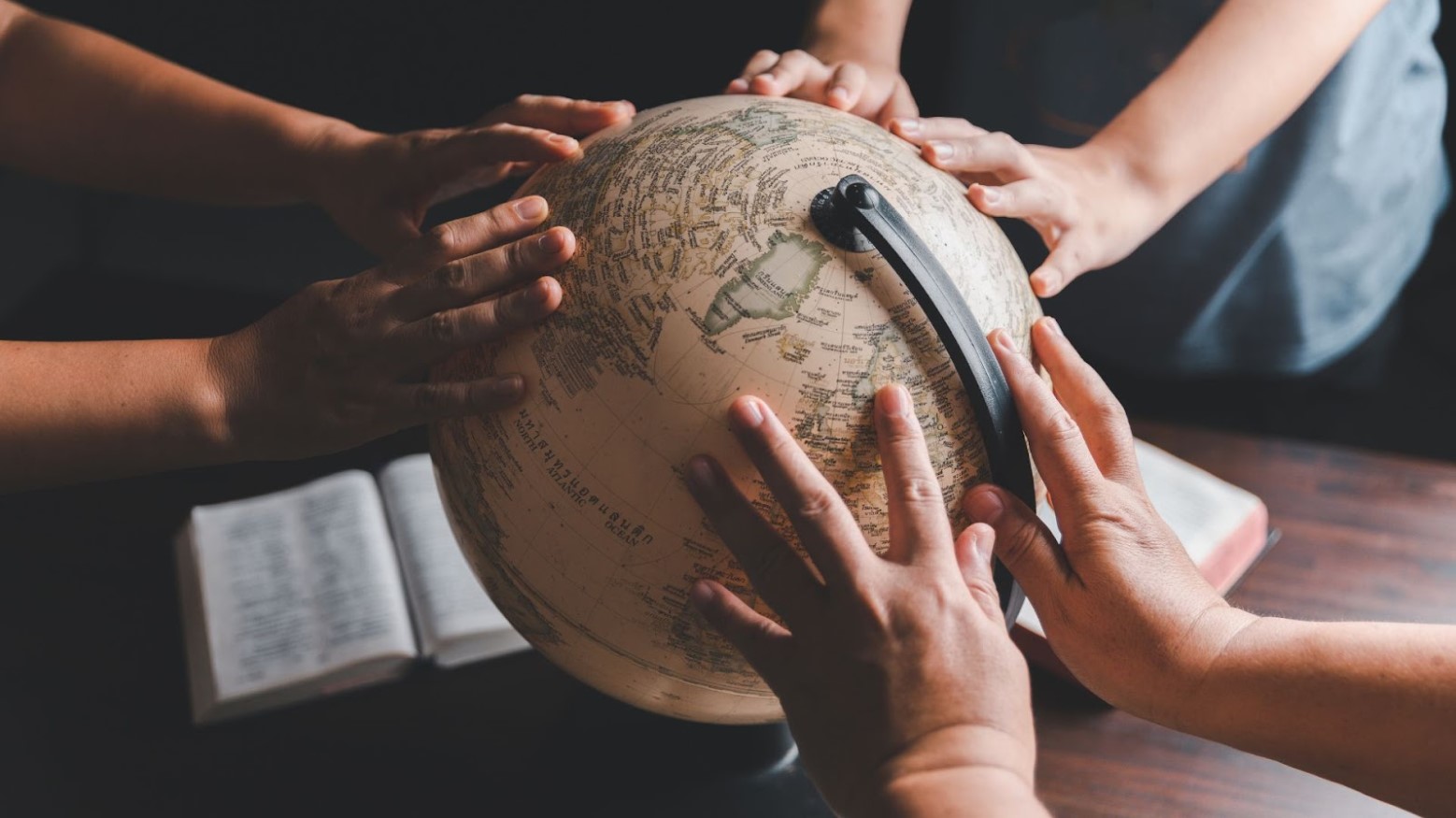 Three young people reach their hands out on a globe